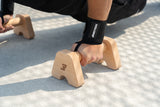 Detailaufnahme: Athlet greift Bmotion Parallettes Small aus Holz bei Push-Up – Fokus auf Handposition, Griffkomfort und Handgelenksbandagen.