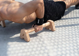 Athlet führt Push-Up auf Bmotion Parallettes Small aus Holz im Outdoor-Setup aus – intensives Eigengewichtstraining mit Handgelenksbandagen (Wrist Wraps) für Brust und Core.