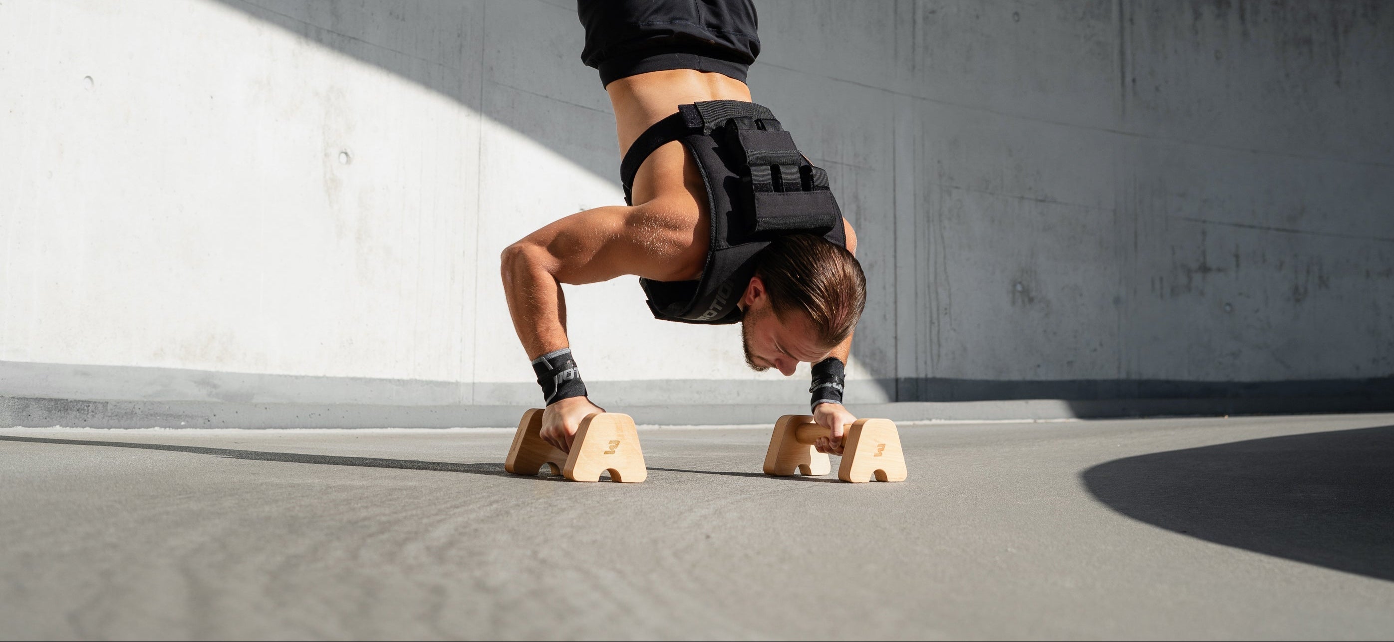 Mann in bmotion Gewichtsweste führt Handstand Push-ups auf Parallettes durch - Calisthenics Training