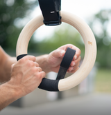 Bmotion Turnringe aus Holz – Hände wickeln Griffband um Holzring im Outdoor-Setup.